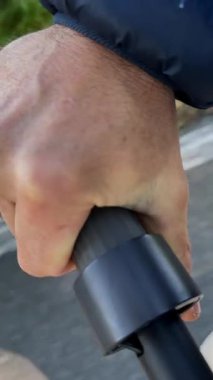 Güneşli bir günde arka planda ağaçlarla parkta yürüyen bir adam. Elleri, yürüyen bir aracın sapını sıkıca kavrıyor. Bu an odaklanmayı ve kararlılığı yakalar..