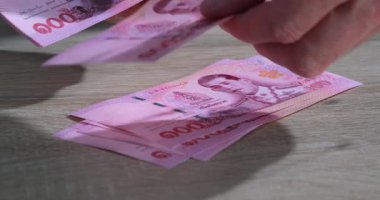 Tahta bir masada el sayımı pembe Tayland banknotları. Ayarlar, muhtemelen gün ışığında bir pazar veya yerel bir dükkanda gerçekleşen mali bir alışverişe işaret ediyor..