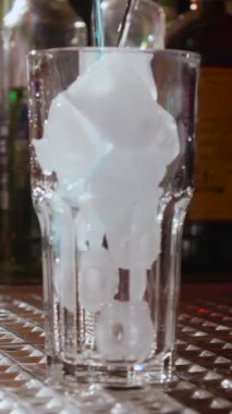 Canlı bir bar atmosferinde duran, sanatsal bir buz formasyonuyla dolu berrak bir bardak. Barmen bu eşsiz görsel buz gösterisini sergilerken ustalıkla bir içki hazırlıyor..