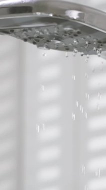 Pürüzsüz bir duş başlığından akan su, doğal ışıkla dolu parlak bir banyoda parıldayan nazik damlacıklar oluşturuyor. Atmosfer taze ve davetkar..