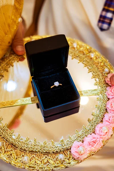 Parlak pırlanta bir nişan yüzüğü, altın ve pembe bir tepside zarif bir şekilde sunulan siyah kadife bir kutunun içinde duruyor. Yansıma parıldıyor, değerli mücevherin parlaklığını arttırıyor..