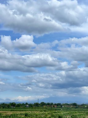 Büyük, büyük, kabarık bulutlar ve güzel, açık mavi bir gökyüzü. Tarlaların ve çayırların arka plan fotoğrafı. Bir tren penceresinden görülmüş. Tasarımın, metnin, mesajların, bilgelik sözlerin, motivasyon kelimelerin için.