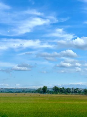 Büyük, büyük, kabarık bulutlar ve güzel, açık mavi bir gökyüzü. Tarlaların ve çayırların arka plan fotoğrafı. Bir tren penceresinden görülmüş. Tasarımın, metnin, mesajların, bilgelik sözlerin, motivasyon kelimelerin için.