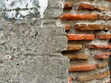 Çimento yüzeyi soyulmuş bir duvar, içeriden çıkan kırmızı tuğlaları ortaya çıkarıyor..