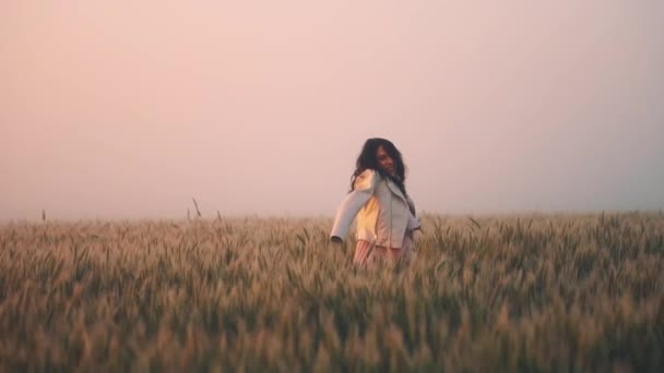 Gravid flicka i en jacka på axlarna, dansande spinning i ett fält av vete — Stockvideo