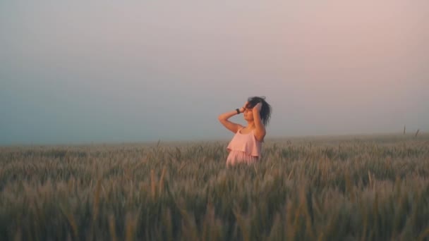 Вагітна дівчина в рожевій сукні дивиться на схід сонця і коригує волосся — стокове відео
