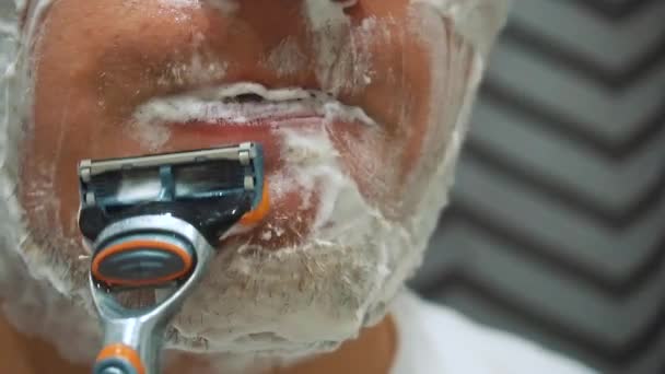 Junger Kerl rasiert sich die Stoppeln im Gesicht mit einem Rasiermesser ab. Verwendet Rasierschaum — Stockvideo