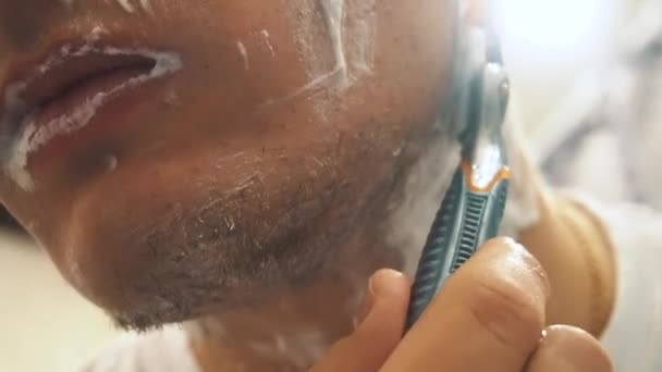 A fiatal fickó borotvával borotválja le a borostát az arcáról. Borotvahab használata — Stock videók