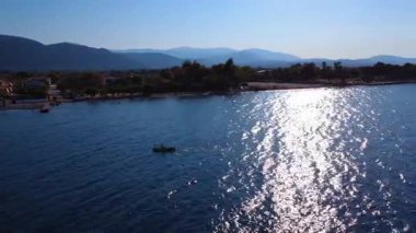 At sunset in Greece, a canoe and sup move through the sea waves, framed by mountains and a wild coastal setting.