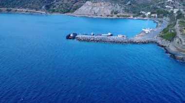 A small harbor on a Greek island in the Aegean shows fishing boats and calm Mediterranean waters. The seaside village rests by the shore.