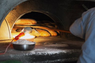 Fırıncı bir somun ekmek ahşap kürekle eski bir fırından alır. Satır taze pişmiş rulo