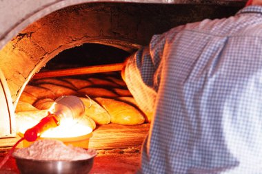 Fırıncı bir somun ekmek ahşap kürekle eski bir fırından alır. Satır taze pişmiş rulo