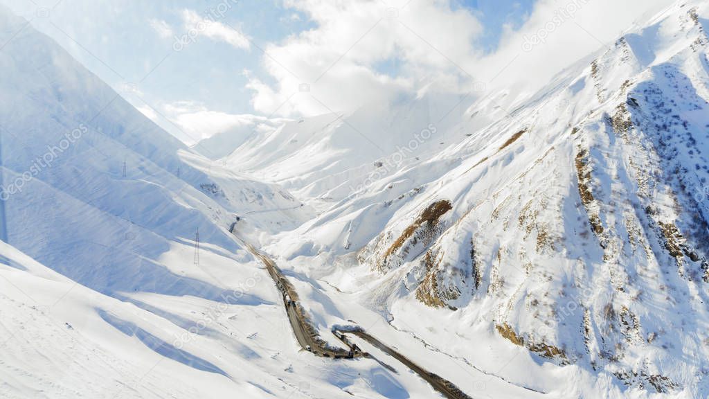 The road to the mountain gorge in winter. Snow-covered slopes of the Caucasus Mountains. Cars move along a winding path through a dangerous pass.