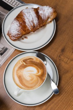 Bir fincan cappuccino kahve ve yakın çekim kruvasan. Lezzetli bir kahvaltı.