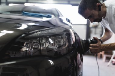 Man with orbital polisher in auto repair shop. Selective focus clipart