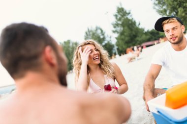 Bir grup çekici genç sahilde eğleniyor, içiyor ve kadeh kaldırıyor..