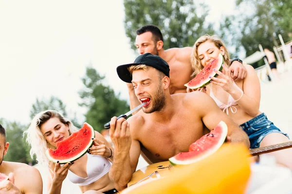 Gençlerin grup karpuz yeme ve kumsalda zevk çekici.