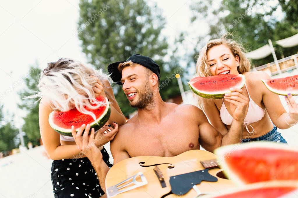 Group of attractive young people enjoying at beach and eating watermelon.