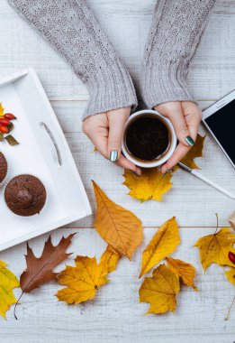 Kahve renkli sonbahar rustik ahşap masada bırakır, smartphone ans çikolata muffins tutan güzel manikürlü eller. Sonbahar ve kış tema. Yukarıdan görüntülemek.