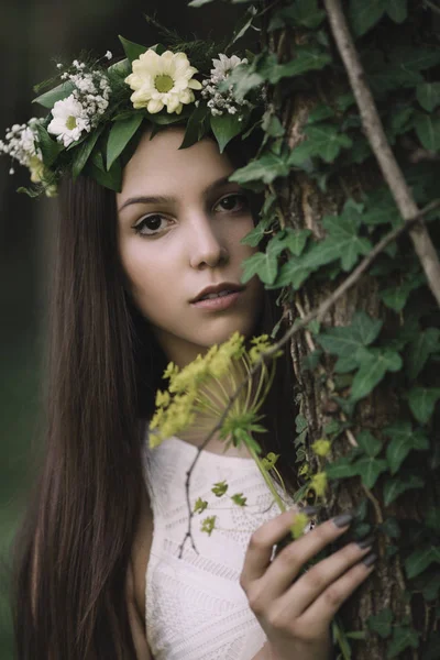 Fine art outdoor portrait of beautiful young woman in a white dress wearing floral wreath