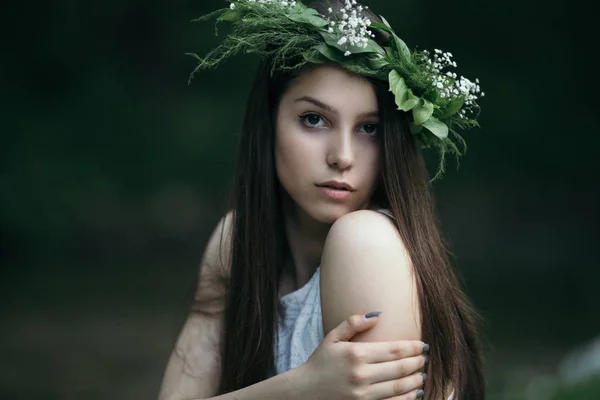 Fine art outdoor portrait of beautiful young woman in a white dress wearing floral wreath