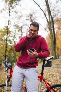 Sonbahar açık havada. Bisiklet Park ile ayakta, bir cep telefonu tutan ve müzik toplama kulaklık genç ciddi yakışıklı adamla izler.