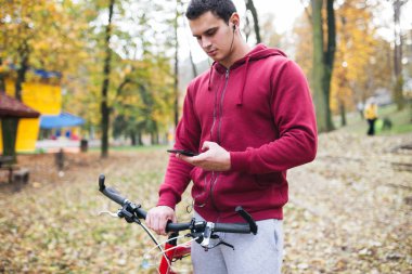Sonbahar açık havada. Bisiklet Park ile ayakta, bir cep telefonu tutan ve müzik toplama kulaklık genç ciddi yakışıklı adamla izler.