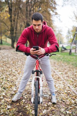 Sonbahar açık havada. Bisiklet Park ile ayakta, bir cep telefonu tutan ve müzik toplama kulaklık genç ciddi yakışıklı adamla izler.