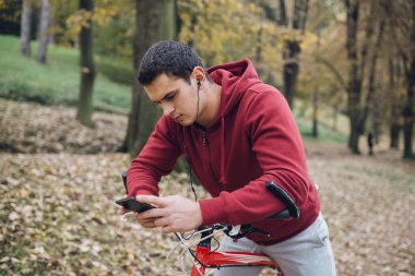 Sonbahar açık havada. Bisiklet Park ile ayakta, bir cep telefonu tutan ve müzik toplama kulaklık genç ciddi yakışıklı adamla izler.