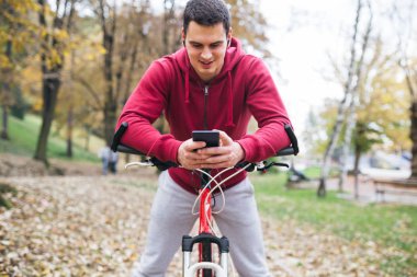 Sonbahar açık havada. Bisiklet Park ile ayakta, bir cep telefonu tutan ve müzik toplama kulaklık genç ciddi yakışıklı adamla izler.
