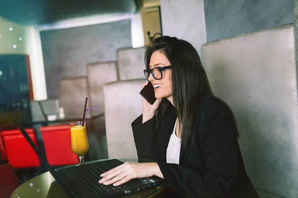 Young attractive business woman sitting in modern cafe restaurant, smiling and looking on her laptop.