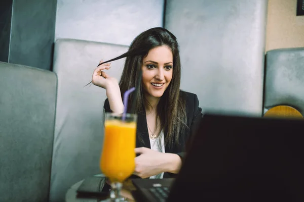 Young attractive business woman sitting in modern cafe restaurant, smiling and looking on her laptop.