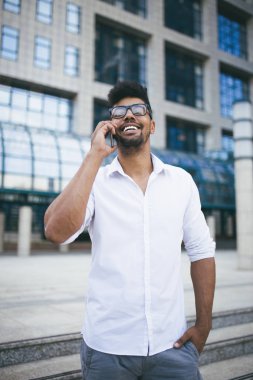 Olumlu ve yakışıklı Afro Amerikalı adam büyük modern iş kurma gülümseyen ve cep telefonuyla konuşurken önünde duran