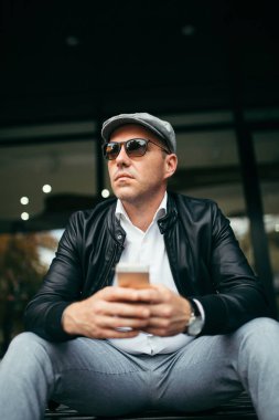 Moda retro giyimli adam şehir sokak ve kullanma telefonla kap ve güneş gözlüğü takıyor