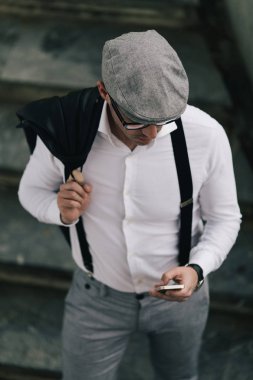 Moda retro giyimli adam şapka ve gözlük şehir sokak ve kullanma telefonla giyiyor