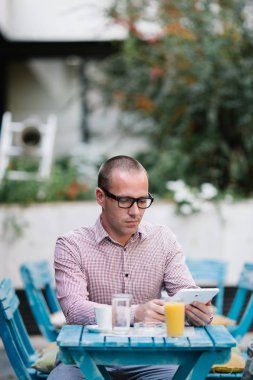 Kafe barda oturmuş, kahve içme ve tablet kullanarak gözlük ile raslantı giyimli adam.