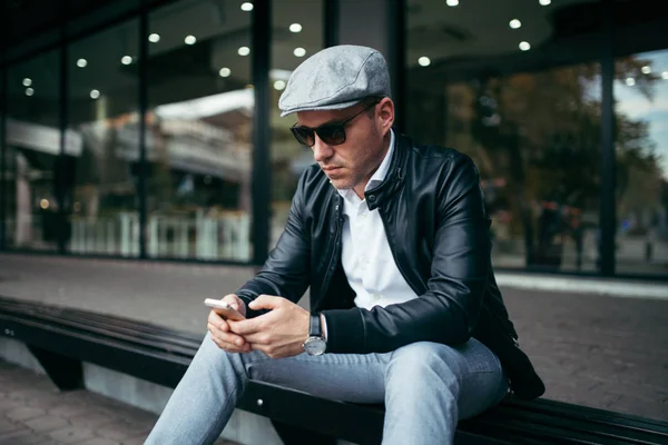 Moda retro giyimli adam şehir sokak ve kullanma telefonla kap ve güneş gözlüğü takıyor