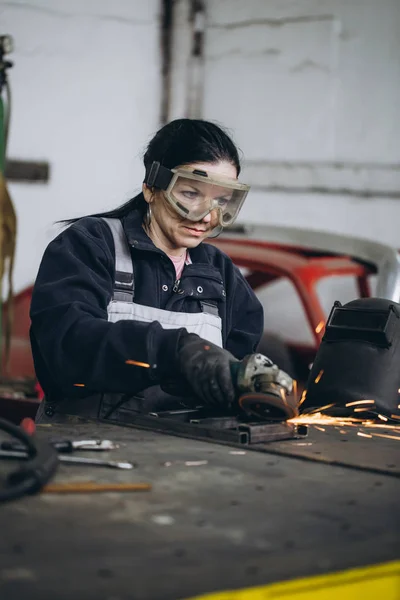 Strong and worthy woman doing hard job in car and motorcycle repair shop. She using grinder to fix some metal bike parts.