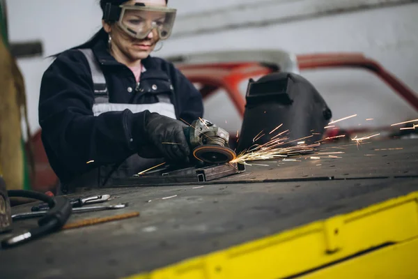 Strong and worthy woman doing hard job in car and motorcycle repair shop. She using grinder to fix some metal bike parts.