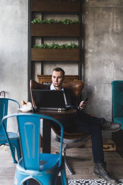 Kafede oturan ve dizüstü bilgisayar, cep telefonu ve tablet işini yapan genç, modern ve olumlu iş adamı.