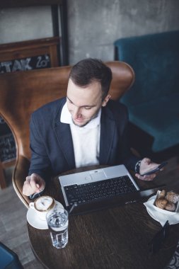 Kafede oturan ve dizüstü bilgisayar, cep telefonu ve tablet işini yapan genç, modern ve olumlu iş adamı.
