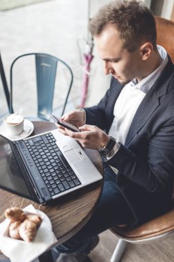 Kafede oturan ve dizüstü bilgisayar, cep telefonu ve tablet işini yapan genç, modern ve olumlu iş adamı.