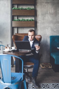 Kafede oturan ve dizüstü bilgisayar, cep telefonu ve tablet işini yapan genç, modern ve olumlu iş adamı.