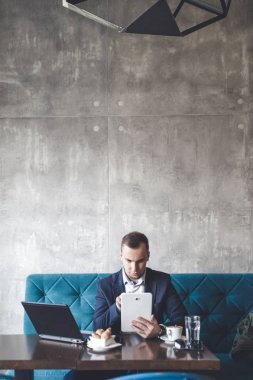 Kafede oturan ve dizüstü bilgisayar, cep telefonu ve tablet işini yapan genç, modern ve olumlu iş adamı.