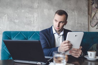 Kafede oturan ve dizüstü bilgisayar, cep telefonu ve tablet işini yapan genç, modern ve olumlu iş adamı.