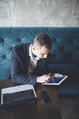 Kafede oturan ve dizüstü bilgisayar, cep telefonu ve tablet işini yapan genç, modern ve olumlu iş adamı.