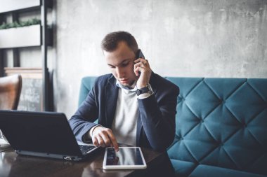 Kafede oturan ve dizüstü bilgisayar, cep telefonu ve tablet işini yapan genç, modern ve olumlu iş adamı.