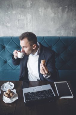 Kafede oturan ve dizüstü bilgisayar, cep telefonu ve tablet işini yapan genç, modern ve olumlu iş adamı.