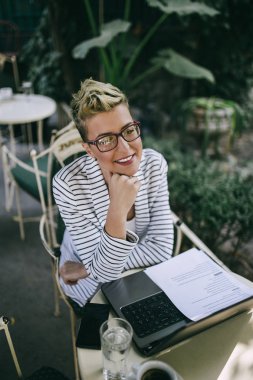 Güzel bahçe cafe bar veya restoran gibi oturan ve onun dizüstü bilgisayarda bir şeyler yapıyor genç mutlu kadın.