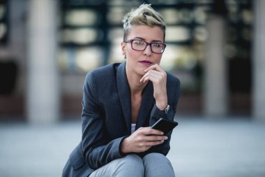 Cep telefonu kullanarak büyük modern binanın önünde genç iş kadını.